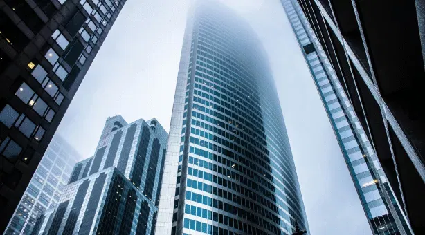 Modern skyscrapers pierce a foggy sky, showcasing impressive architecture and urban development.