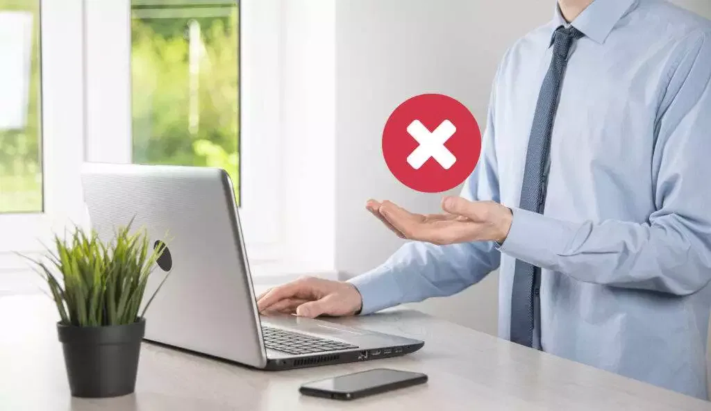 Businessperson gesturing rejection near laptop; red X symbol. ASIC license cancellation concept.