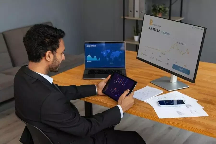 Businessman analyzing financial data on multiple screens and a tablet.