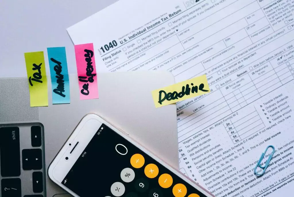 Tax form, calculator, and smartphone showing a calculator app; deadline reminder note.