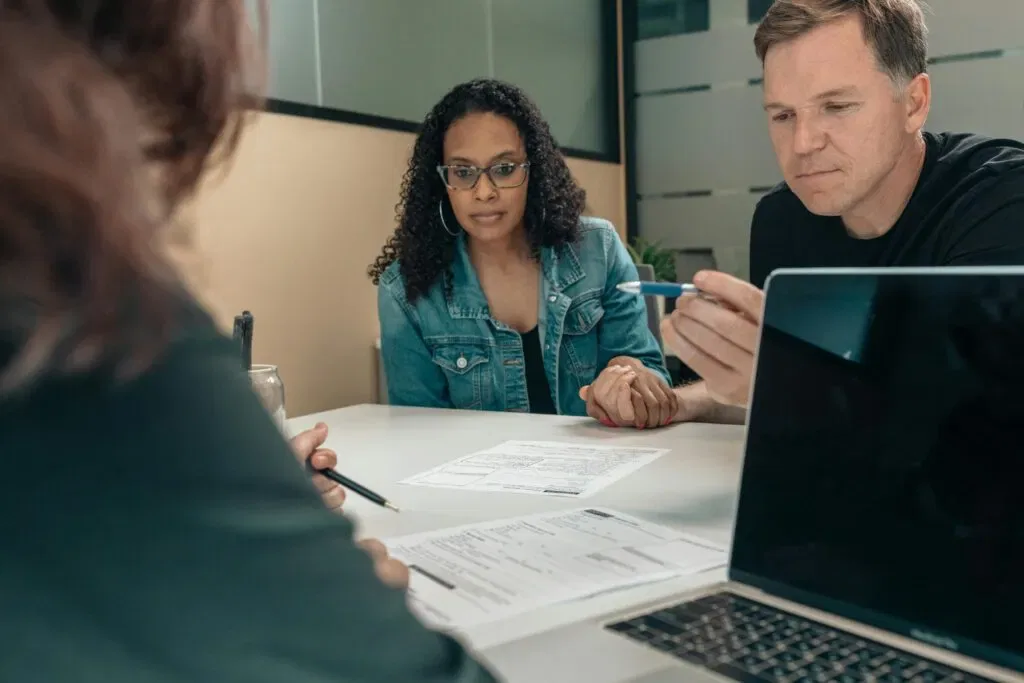 People discussing FSG requirements around a table with documents and a laptop, focusing on collaboration and decision-making.
