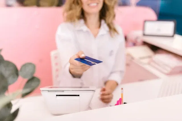Woman handing over a credit card at a reception desk, representing payments in Australia.