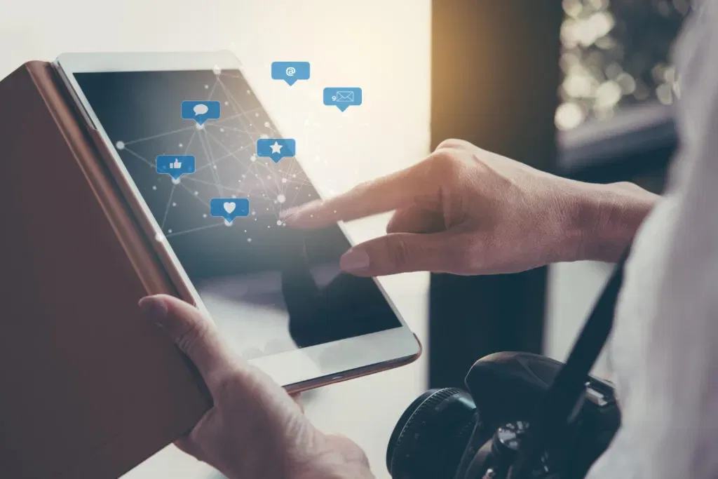 Person using a tablet with social media icons, camera nearby. Understanding digital communication.