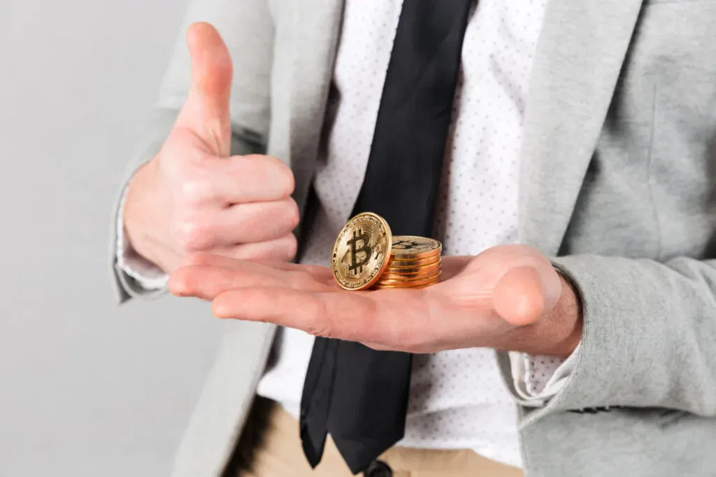 Man in suit holding Bitcoin coins and giving a thumbs up. Crypto assets.