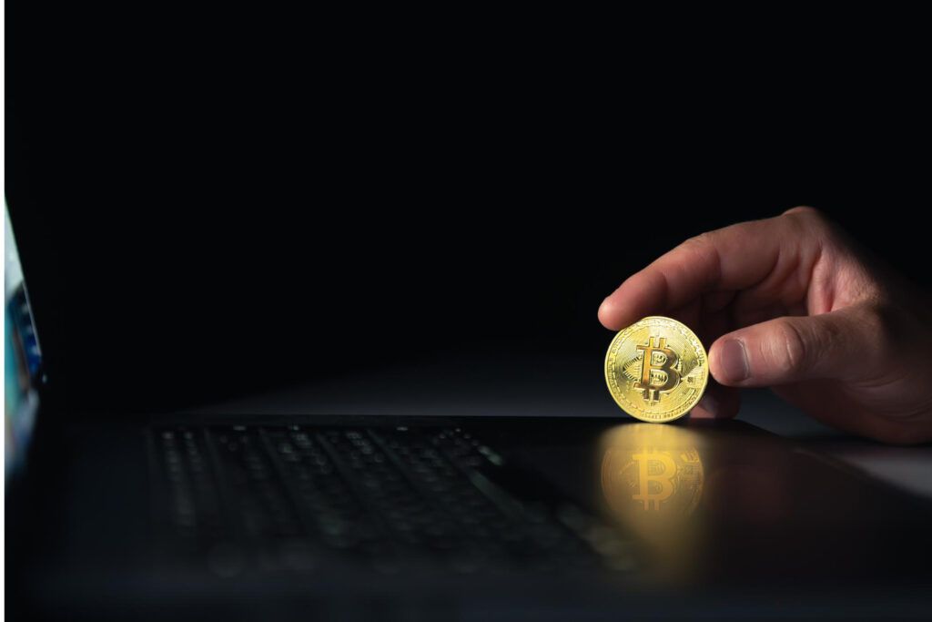 Hand holding Bitcoin over laptop, reflecting on screen. Digital asset concept.