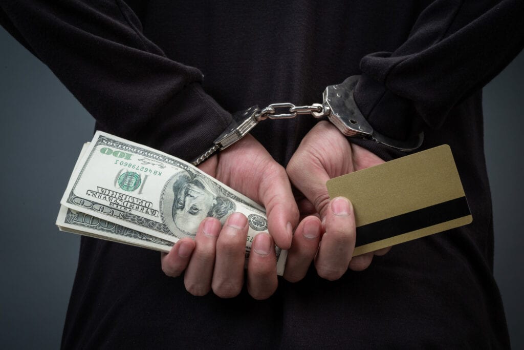 Man in handcuffs holding cash and credit card, money laundering concept