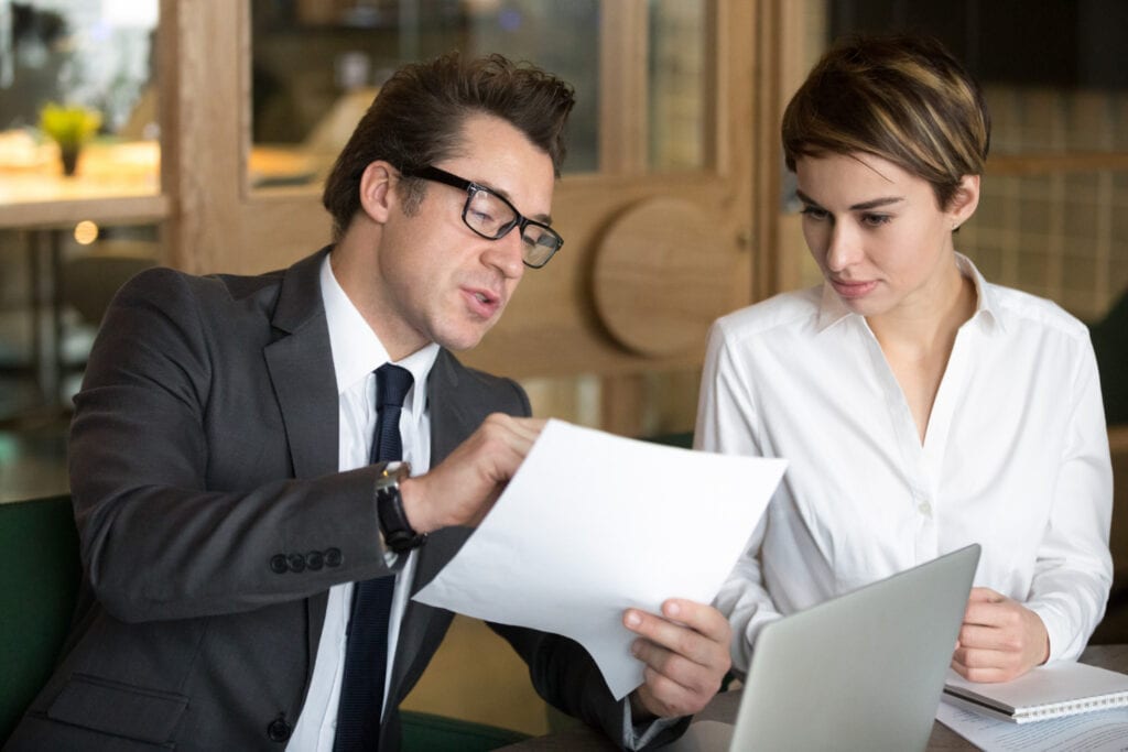 Business professionals reviewing documents and laptop, discussing ASIC RG 181 compliance.