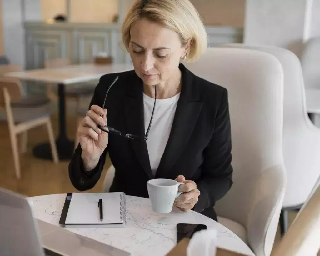 Businesswoman reviewing documents at cafe, holding coffee cup.