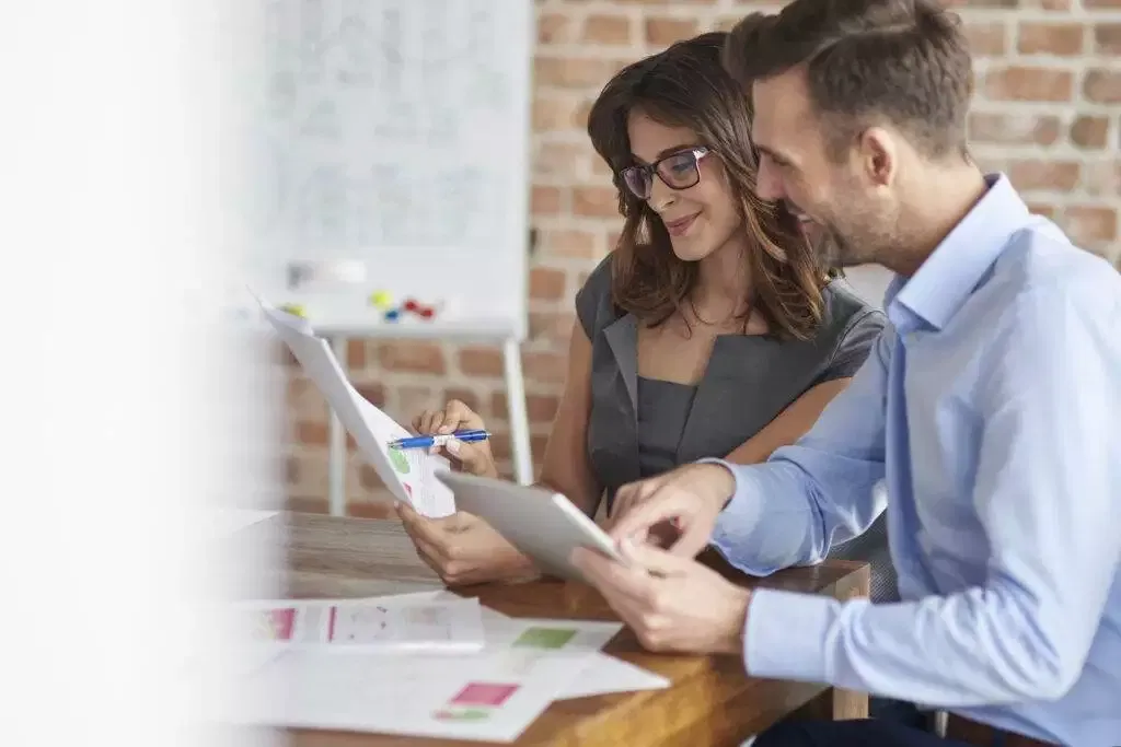 Two business colleagues review financial documents and a tablet, discussing an Australian Financial Services Licence application.