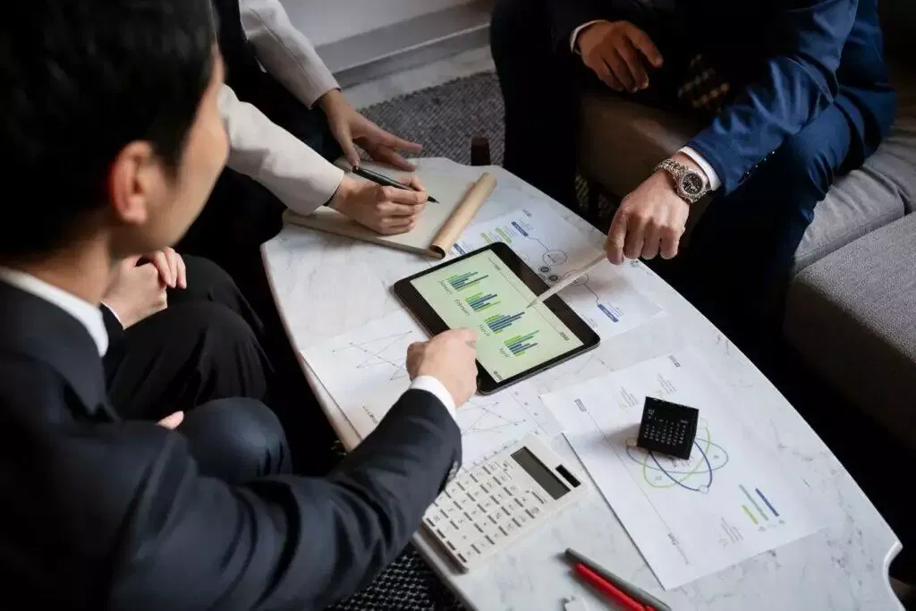 Businesspeople review financial charts on a tablet during a meeting, discussing a managed investment scheme.