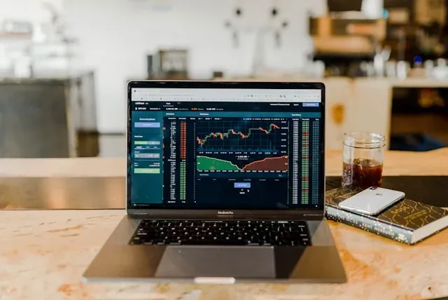 Laptop displaying stock market data, phone, and notebook on a desk.