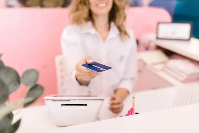 Woman handing over a credit card at a reception desk, representing payments in Australia.