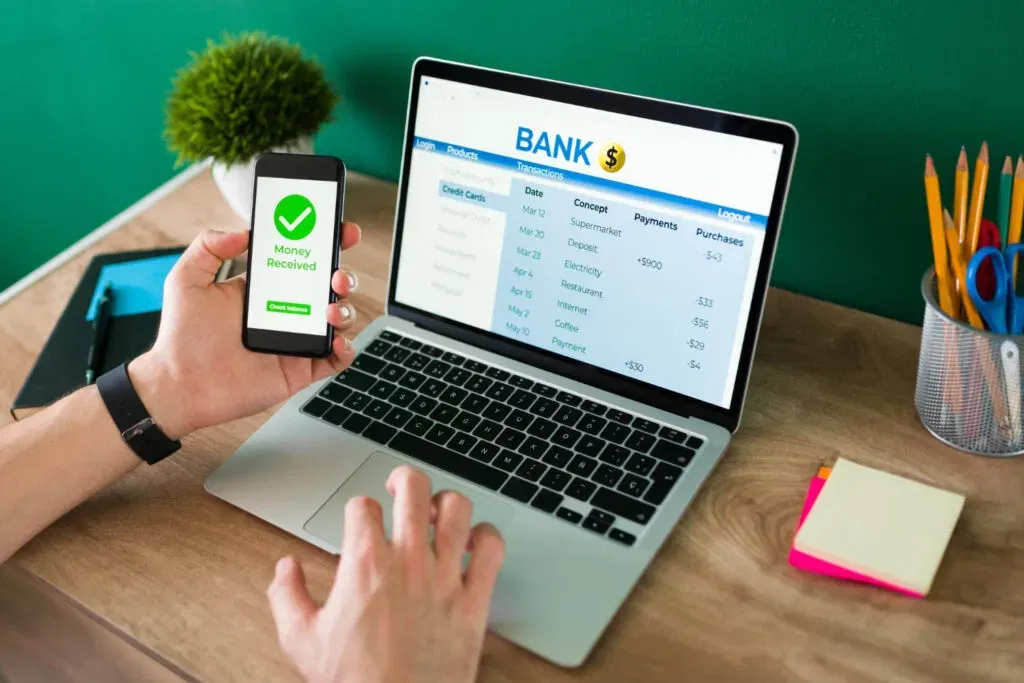 Online banking: Person using a laptop to view transactions and a phone showing 