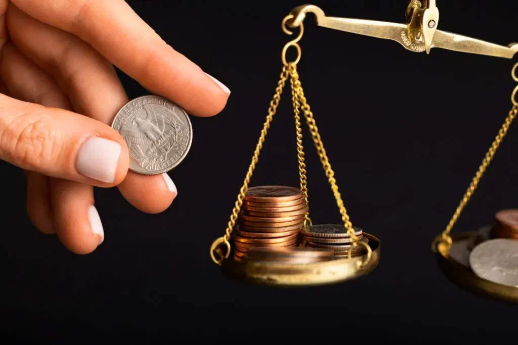 Coins on a balance scale, with a hand holding a quarter.