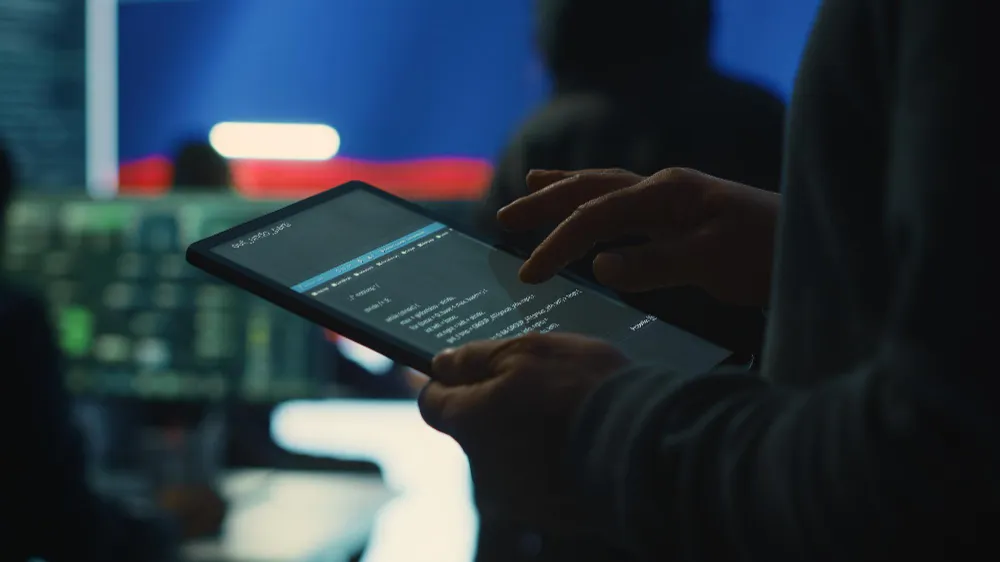 Close-up of hands using a tablet displaying code, cybersecurity concept.