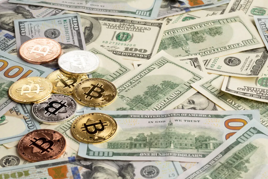 Bitcoin coins scattered on US Dollar bills. Crypto and traditional currency.